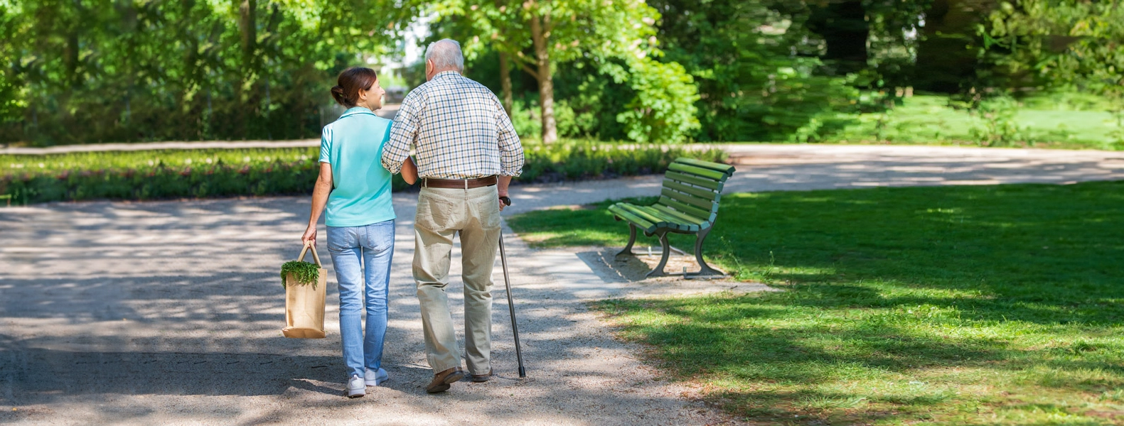 En ung kvinna promenerar med en gammal man i parken. Kvinnan bär en kasse med livsmedel.